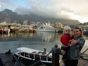 Vrouw houdt een jong kind vast bij een haven met boten, een stad, een groot jacht en bewolkte bergen op de achtergrond in Zuid-Afrika