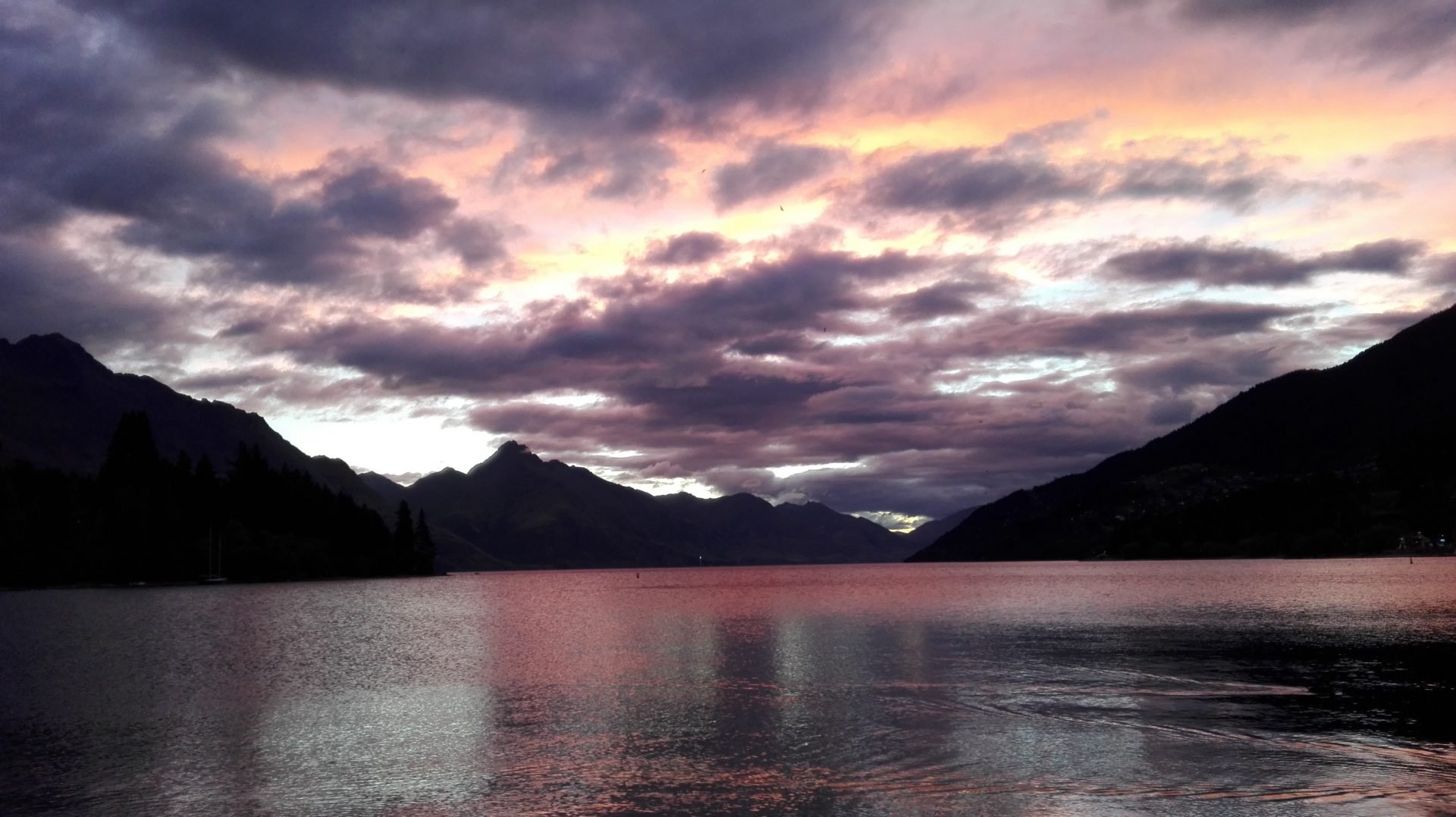 Meer omringd door bergen onder een dramatische zonsondergang met paarse en oranje wolken in een bergachtig natuurgebied