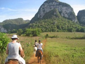 Drie ruiters rijden te paard over een zandpad door een groene vallei met steile rotsbergen in Viñales Cuba