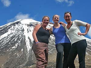 Drie lachende vrouwen poseren voor een besneeuwde berg onder een blauwe lucht in een bergachtig natuurgebied