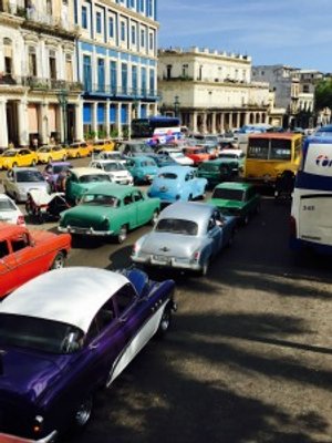Veel kleurrijke klassieke auto’s rijden over een drukke straat in Havana in Cuba