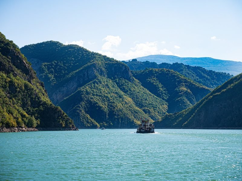 Veerboot op een turquoise meer in Albanië tussen steile groene bergen