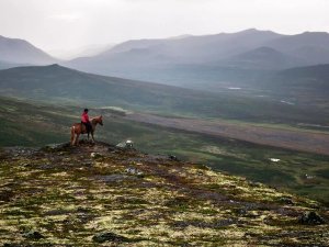 Person on horseback on a rocky hill overlooking a vast, hazy mountain landscape.
