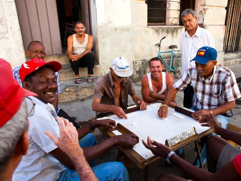 Een groep mannen speelt domino en lacht buiten in Cuba