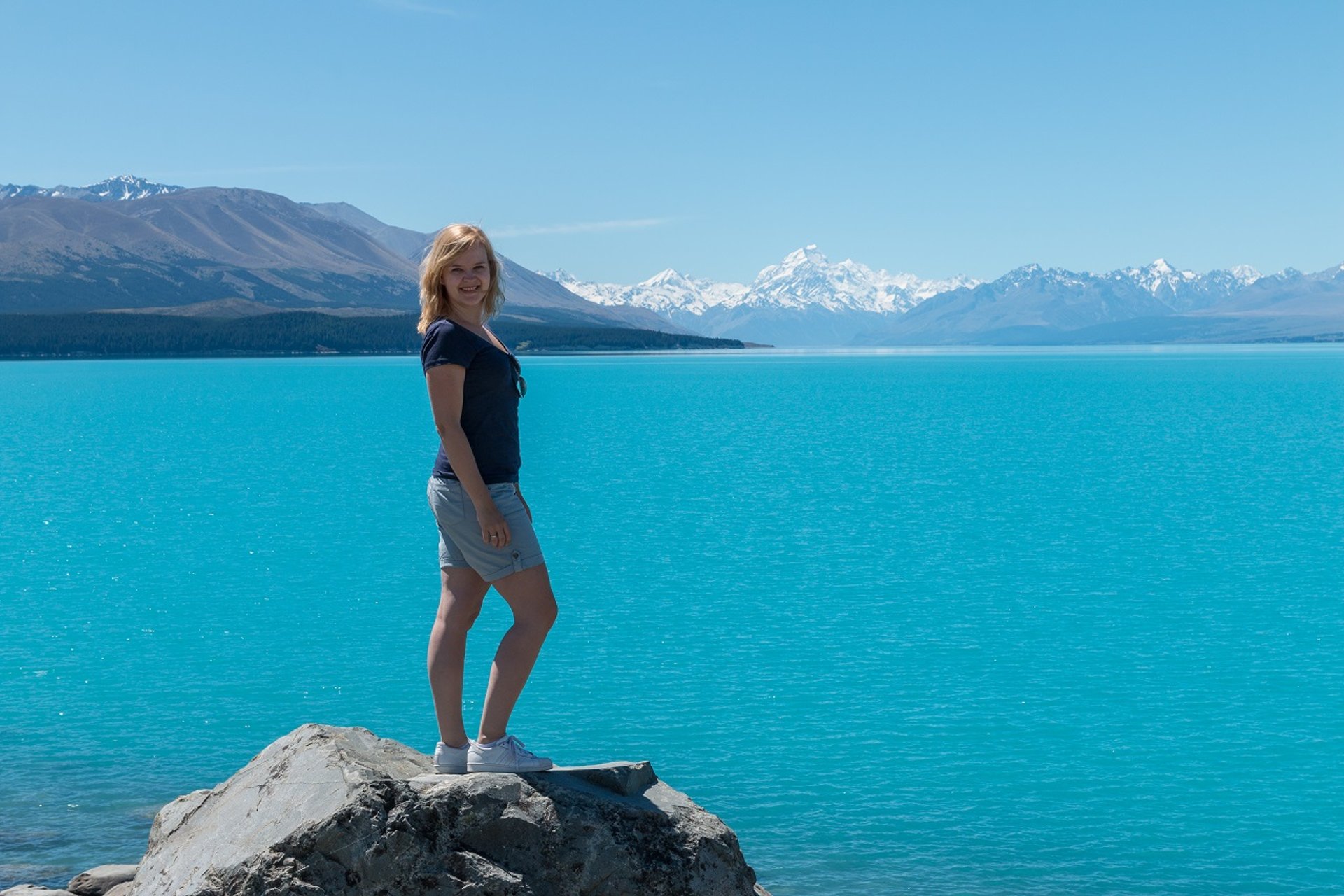 Vrouw bij een fel turquoise meer met besneeuwde bergen op de achtergrond in een bergachtig natuurgebied