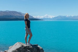 Vrouw bij een fel turquoise meer met besneeuwde bergen op de achtergrond in een bergachtig natuurgebied