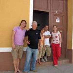 Vijf reizigers lachen samen voor een geel gebouw met houten deuropening in Trinidad Cuba