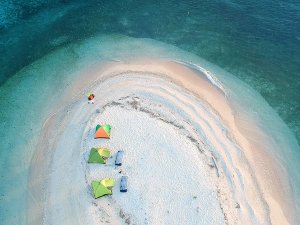 Luchtfoto van een klein zandstrand in zee met drie gekleurde tenten en enkele ligbedden.