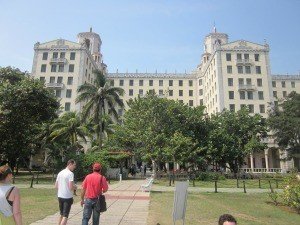 Het statige lichte Hotel Nacional de Cuba met twee torens gezien vanuit de tuin waar mensen over een pad lopen in Havana in Cuba