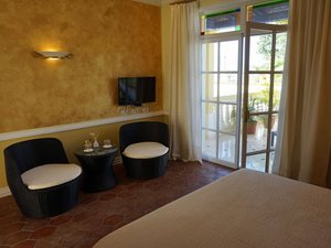 Een slaapkamer met gouden muren, een terracottavloer, een zithoek met een tv en openslaande deuren naar een balkon in Cuba