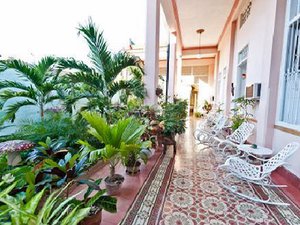 Lang buitenterras met weelderige tropische planten, een vloer met patroontegels en witte metalen schommelstoelen in Cuba