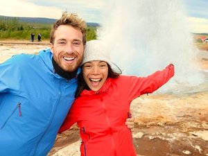 Lachende man en vrouw voor een uitbarstende geiser in IJsland