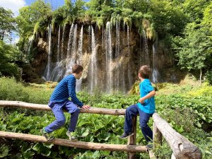 Twee jongens zitten op een houten hek en kijken naar een grote waterval in Kroatië