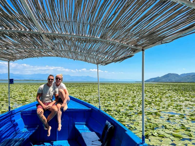 Lachend stel in een blauwe boot met rieten dak op een meer vol waterlelies, met bergen op de achtergrond in Kroatië