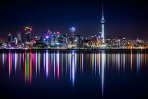 Stadsbeeld van Auckland bij nacht met de Sky Tower en kleurrijke lichtreflecties in het water aan de kust in Nieuw-Zeeland