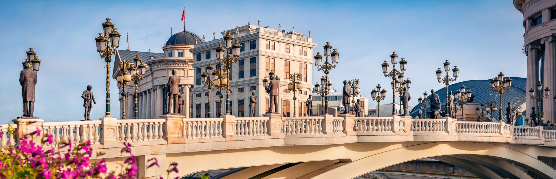 Sierlijke brug met standbeelden en lantaarnpalen, omringd door klassieke gebouwen onder een blauwe lucht in Skopje in Noord-Macedonië