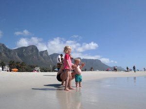 Gezin met twee jonge kinderen op een zonnig strand, met bergen op de achtergrond in Zuid-Afrika