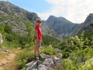 Kind in wandelkleding staat op rotsen in een bergvallei in Kroatië
