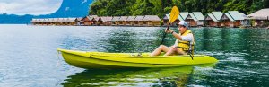 Man kajakkend door Cheow Lan Lake in Khao Sok, Thailand. Op de achtergrond zie je bungalows op het water.