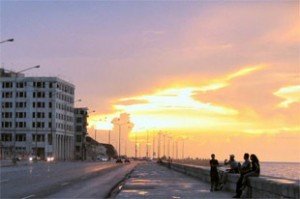 Kleurrijke zonsondergang boven de kust met mensen op de Malecón en weg langs gebouwen in Havana Cuba