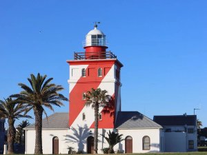Rood-wit gestreepte vuurtoren met witte koepel, omringd door palmbomen onder een heldere blauwe lucht in Zuid-Afrika