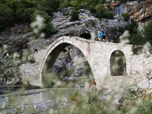 Oude stenen boogbrug in Albanië over een rotsachtige rivier met mensen die erop en ernaast lopen