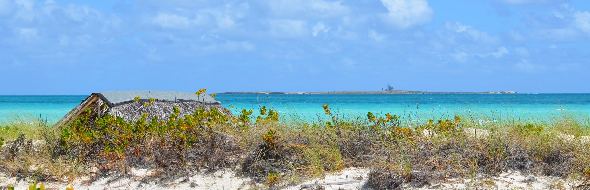 Rustieke rieten hut op een zandduin met uitzicht over een turquoise zee en een vaag eiland in de verte in Cuba