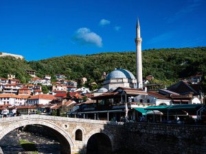 Historische stenen boogbrug in Prizren in Kosovo naar een stad met koepelmoskee, hoge minaret en huizen op een groene heuvel