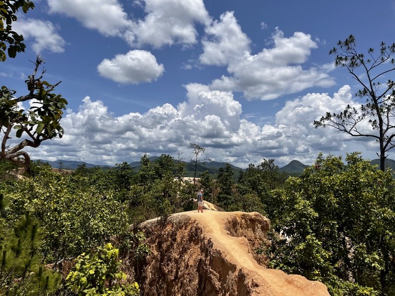 Wandelaar op de smalle zandstenen rots kam van Pai Canyon in Noord-Thailand, omringd door groene jungle en met uitzicht op beboste bergen onder een blauwe lucht vol wolken.