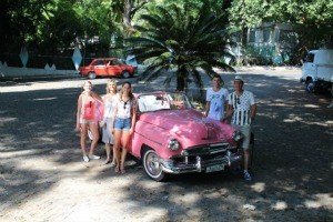 Zes mensen poseren naast een felroze vintage cabrio in Havana in Cuba