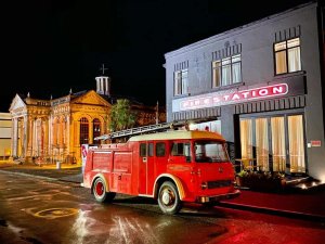 Vintage rode brandweerwagen staat op een natte straat bij nacht voor een gebouw met een FIRESTATION neonbord in de stad