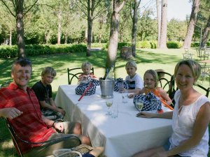Lachend gezin van zes met twee volwassenen en vier kinderen geniet van een maaltijd aan een witgedekte tafel in een zonnige tuin in Zuid-Afrika