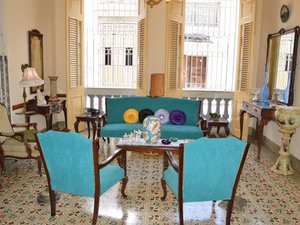 Een levendige woonkamer in Cuba met tealgekleurde stoelen en bank, een kleurrijke vloer met patroontegels en open ramen met luiken.