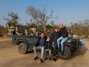 Lachend gezin van vier poseert bij een open safaritruck in een savannelandschap in Zuid-Afrika