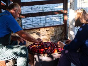 Twee mensen roosteren rode paprika’s in een grote pan buiten in Albanië
