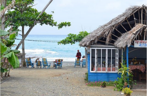Blauwe strandhut met rieten dak op een zandstrand waar mensen ontspannen op stoelen met uitzicht op de zee in Cuba