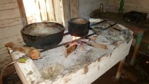 Twee grote pannen koken boven een open vuur op een rustieke haard in een houten ruimte in Cuba