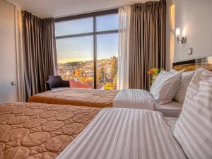Hotelkamer in Ohrid in Noord-Macedonië met twee bedden en groot raam met uitzicht op de stad bij zonsondergang