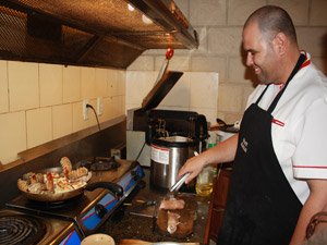Lachende chef die kreeft en andere gerechten bereidt op een fornuis in een keuken in Havana, Cuba