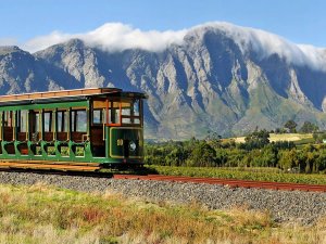 Groene vintage tram op rails met een bergketen vol wolken en wijngaarden op de achtergrond in Zuid-Afrika