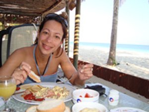 Lachende vrouw die eet aan een tafel aan het strand in Varadero, Cuba met de oceaan op de achtergrond