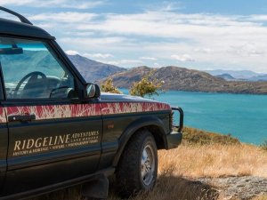 Ridgeline Adventures SUV kijkt uit over het turquoise Lake Wanaka met bergen op de achtergrond in Nieuw-Zeeland