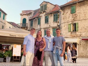 A family of four smiles on a historic street with stone buildings and a restaurant called Tavern Favola.