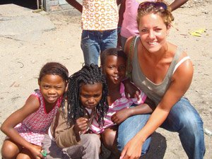 Lachende vrouw knielt buiten op stoffige grond met vier jonge kinderen in Zuid-Afrika