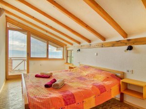 Slaapkamer in Albanië met oranje sprei, schuin plafond met houten balken en grote ramen met uitzicht op zee