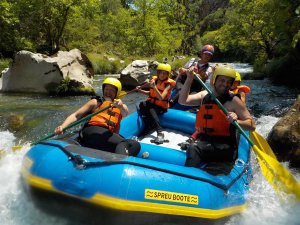 Groep lachende mensen in een blauwe raft met helmen en reddingsvesten peddelt door stroomversnellingen op de Soča-rivier in Slovenië