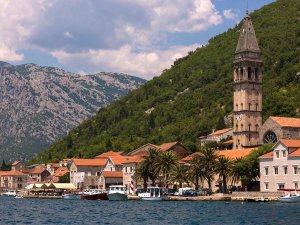 Kustplaats met stenen kerktoren, rode daken en boten aan het water tegen steile groene bergen in Kroatië