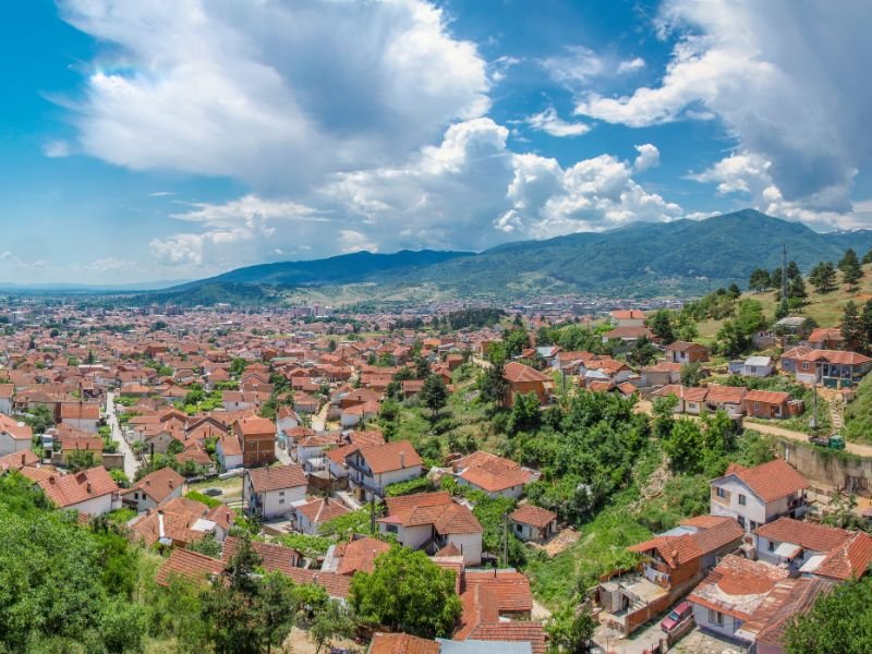 Luchtfoto van een stad met huizen met rode daken in een vallei, omringd door bergen onder een blauwe lucht met wolken in Bitola in Noord-Macedonië