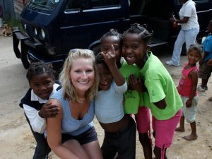 Lachende blonde vrouw omringd door blije zwarte kinderen, waarvan sommigen haar knuffelen in Zuid-Afrika