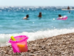 Roze strandemmer en speelgoed op een kiezelstrand met zwemmers in de blauwe zee op de achtergrond in Kroatië